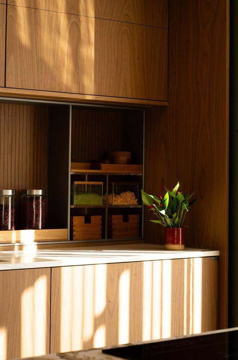 Detalhe de cozinha em lâmina de madeira com veio contínuo entre as portas e luz natural rasante, projeto Marel