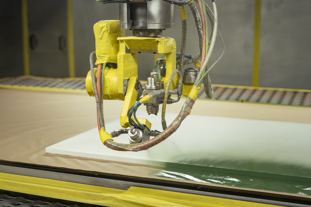 Braço robótico aplicando laca sobre painel na cabine de pintura da fábrica própria da Marel