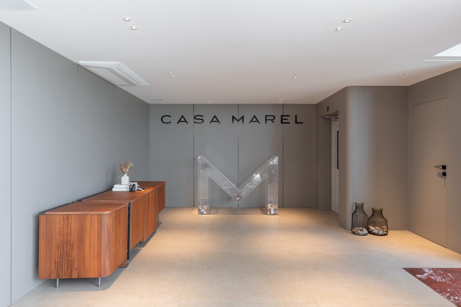 Recepção da Casa Marel em Alphaville, com aparador em madeira e o letreiro Casa Marel na parede